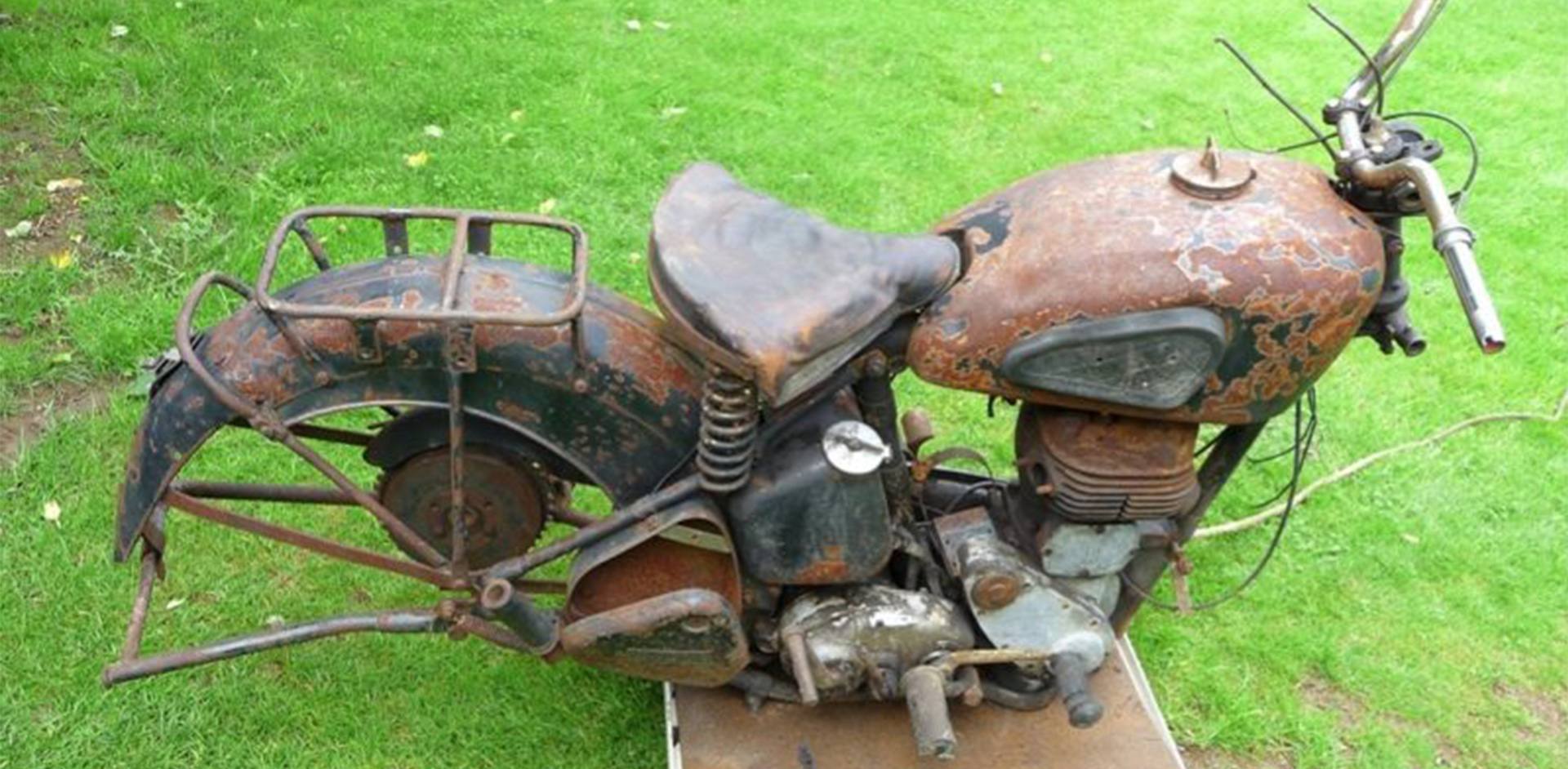 Incomplete, heavily patinated BSA KM21 motorcycle photographed from above on grass.